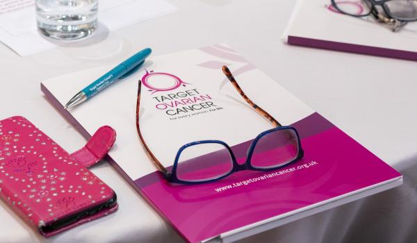 A Target Ovarian Cancer booklet with a pair of glasses on top and a phone next to it in a pink case