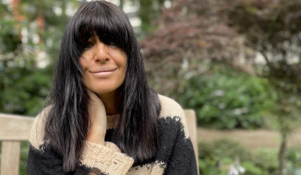 Claudia Winkleman sitting on a park bench looking into the camera