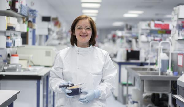 An ovarian cancer researcher smiling and holding lab equipment