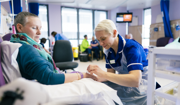 Woman with ovarian cancer in a treatment room looking down as a nurse provides chemotherapy