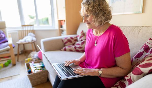 A person in a pink tshirt sitting on the sofa reading her laptop screen