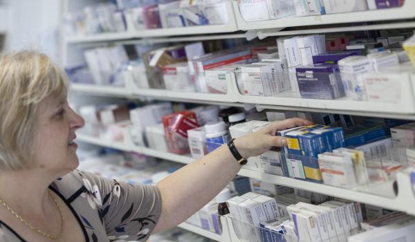 An image of a person working in a pharmacy taking a box of pills from the shelf