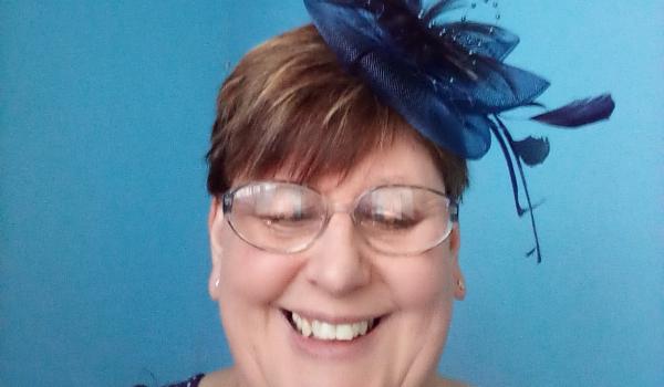 Amanda smiling wearing a blue fascinator in her hair