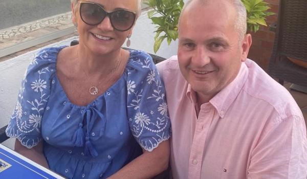 Pauline and Declan sitting in a restaurant with his arm around her smiling