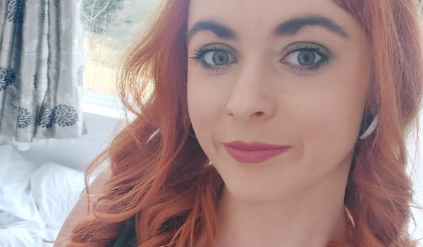 A selfie of Lucy with red curled hair and a teal green top on 