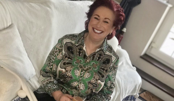 Alison smiling sitting on the sofa holding a cup of tea