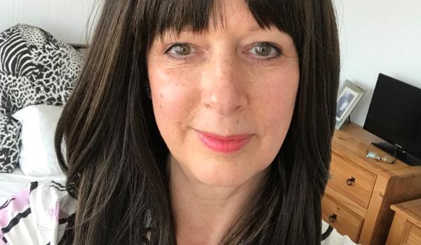 Gillian with long dark hair and a fringe taking a selfie, she's wearing her wig she named "Cher" 