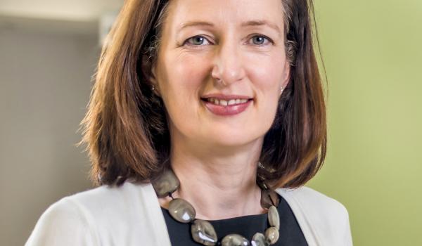 A headshot image of Professor Fiona Thistlethwaite wearing a dark top, white cardigan and necklace