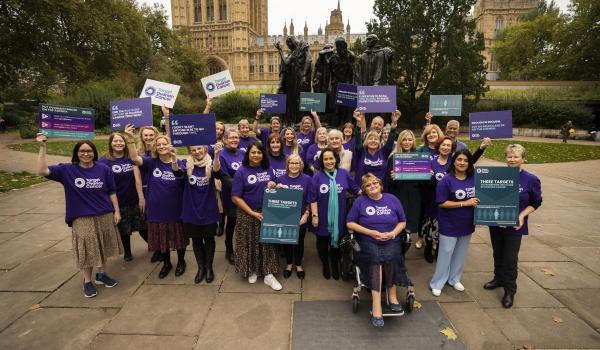 A group of Target Ovarian Cancer campaigners standing in the gardens in front of Westminster Parliament 
