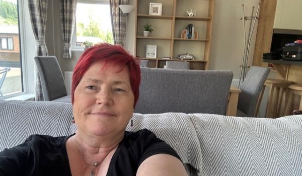 Lorraine, a lady with red hair sitting on her sofa taking a selfie and smiling