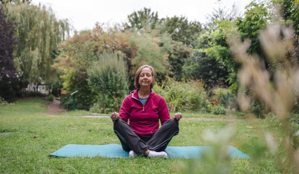 A woman in the park practicing yoga on a teal coloured yoga mat