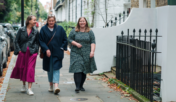 Three women walking down the street together all chatting a smiling