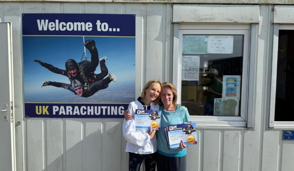 Two women with their arms around each other in front of UK Parachuting's office holding up  their certificates