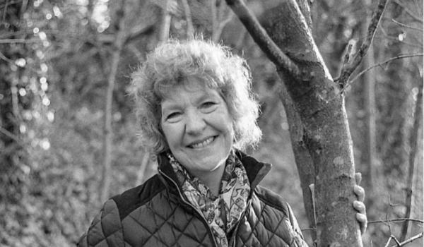 A black and white photo of Gill smiling, she has short curly hair and is wearing a dark coloured quilted jacket