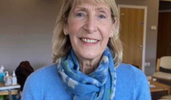 A photo of Sue smiling wearing a blue long sleeved top and blue patterned scarf