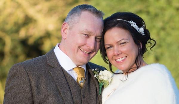 Carl and Fiona on their wedding day, with their heads close together smiling