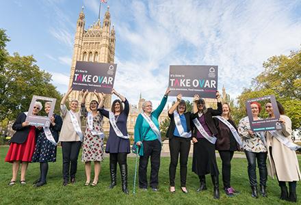 Women with their arms raised, holding up placards outside parliament supporting Target Ovarian Cancer's TAKE OVAR campaign