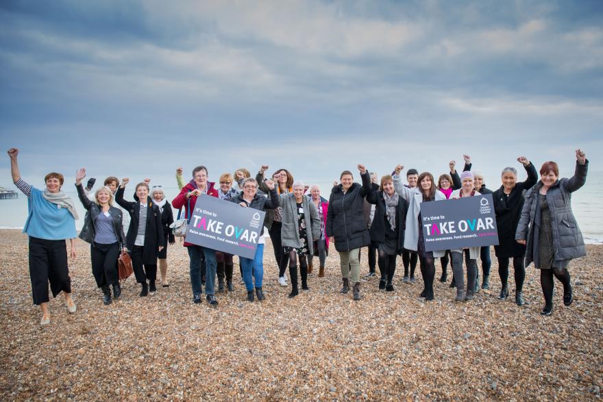 Women with their arms raised and holding placards at Brighton beach supporting Target Ovarian Cancer's TAKE OVAR campaign
