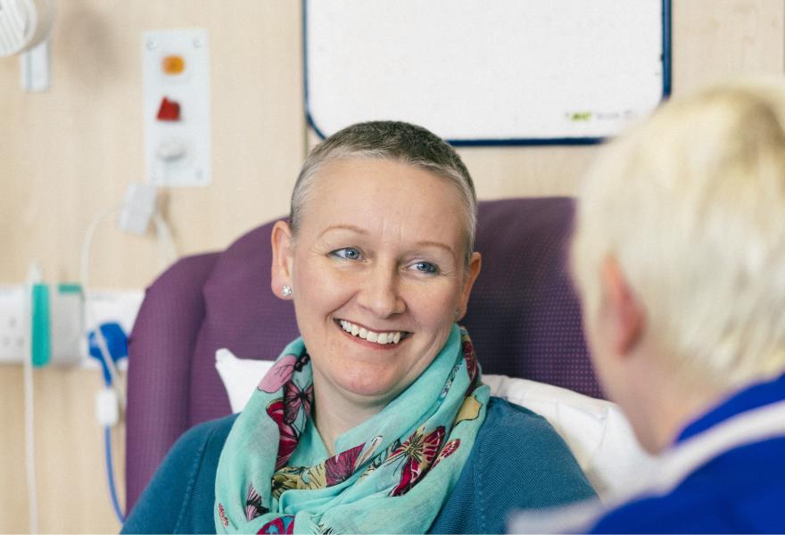 A woman with ovarian cancer smiling and talking to a nurse during chemotherapy