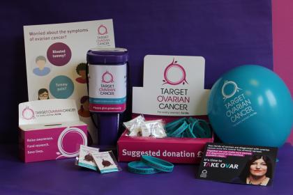 An array of Target Ovarian Cancer fundraising and awareness materials, including a collection box, collection tin, balloon, pin badges, wristbands, leaflets and posters