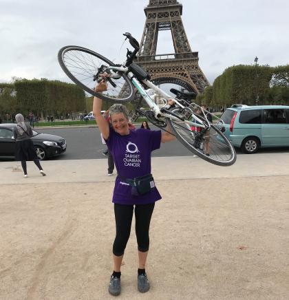 Sara, a Target Ovarian Cancer fundraiser, holding her bike up in the air in front of the Eiffel Tower