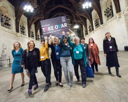 Target Ovarian Cancer campaigners walking through parliament holding a TAKE OVAR placard