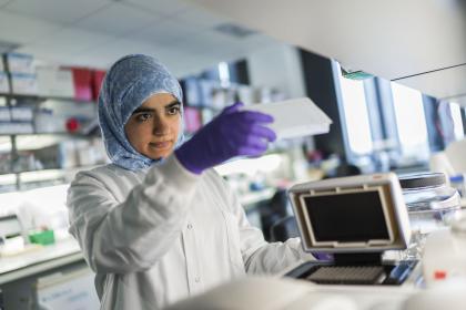 A female ovarian cancer researcher wearing a headscarf, purple gloves and a lab coat using equipment
