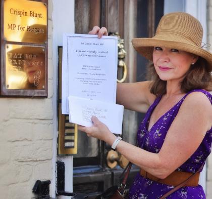 Woman holding up an invitation whilst standing outside the door of an office