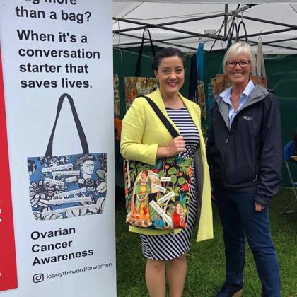A campaigner and her MP wearing a bag standing next to a sign