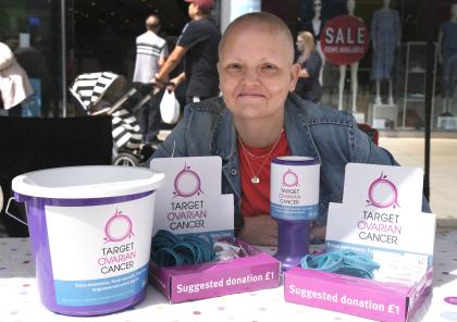 Katy sitting at a table with Target Ovarian Cancer collection buckets and other fundraising materials