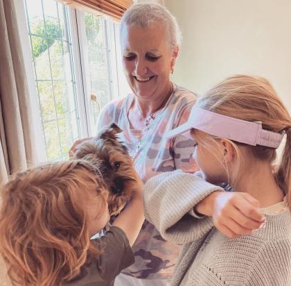Denise smiling pictured with her puppy and grandchildren