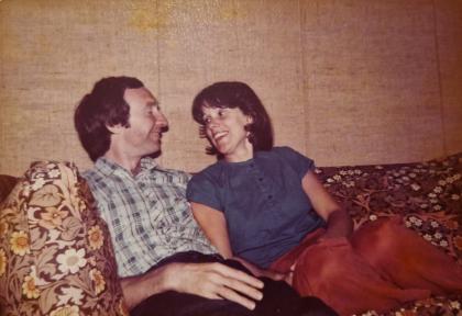 Caroline and her husband Ralph when they were younger sitting on a sofa smiling at each other