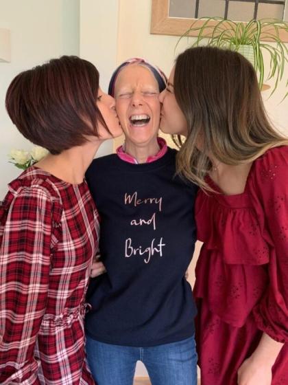 Gaby and Chloe standing either side of their mum Amanda kissing her cheeks whilst Amanda has a huge smile