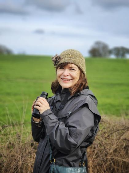 Annie standing in a field wearing a hat and coat, smiling to the camera