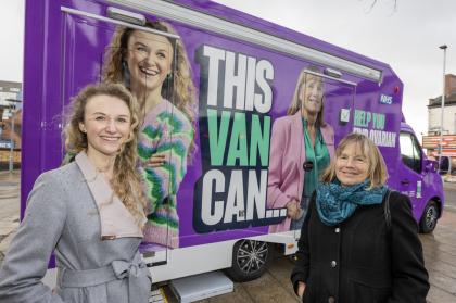 A photo of Charlotte and Hilary standing in front of a purple van that has their photographs on the side and the words This Van Can