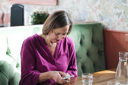 A woman wearing a purple top sitting at a table on her phone