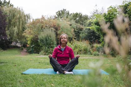 A woman in the park practicing yoga on a teal coloured yoga mat