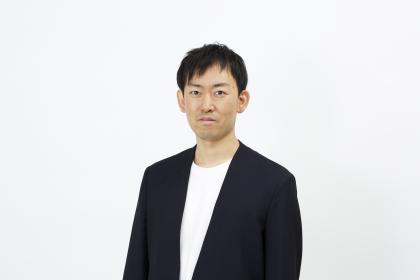 A headshot of Jun Ishihara wearing a black blazer and white tshirt looking straight at the camera