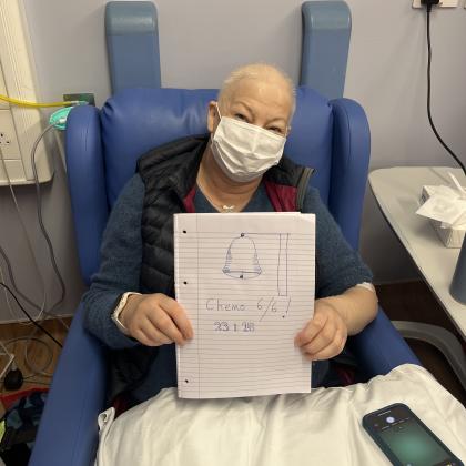 Wendy in hospital after her final chemo session. She is wearing a mask and holding up a sign that say 6/6