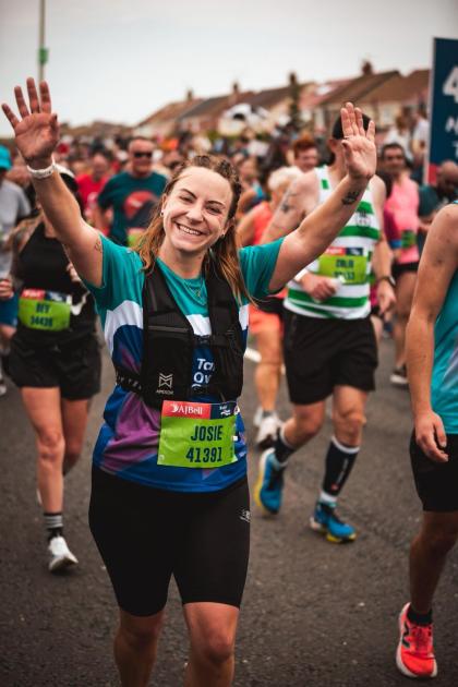Josie running the Great North Run smiling and waving both of her arms in the air