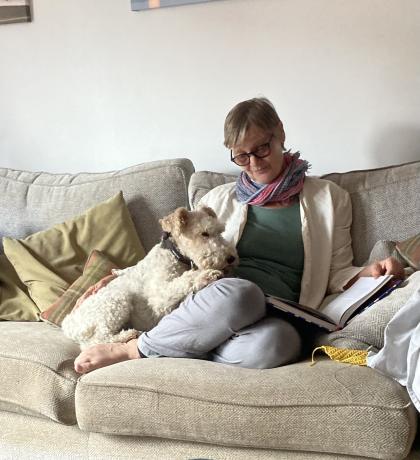 Nicola sitting on the sofa reading with her dog resting it's head on her thigh