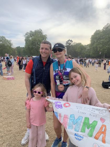 Hannah standing in her Target Ovarian Cancer running vest with her London Marathon medal one, smiling with her husband and two young daughters