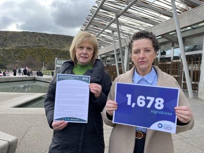 Two women holding up placards outside Scottish Parliament