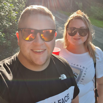 Edd and his partner Sophie smiling to camera, both wearing sunglasses.